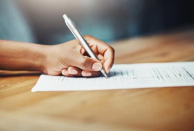 A hand holding a pen and filling out an application form