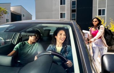 Two individuals in a stationary car as another person gets in the backseat.