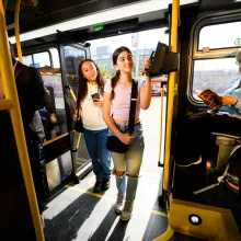 Two teens scanning their smartphone based transit cards as the board a bus