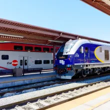 A sleek blue train pulling into a train station next to a red and white train