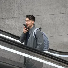 A man speaking into his phone mic while riding an escalator