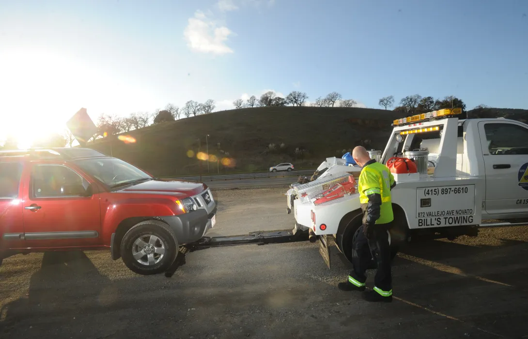 A towtruck operator hooks up a disabled red SUV to a towtruck with a 511 Freeway Assist logo on the door