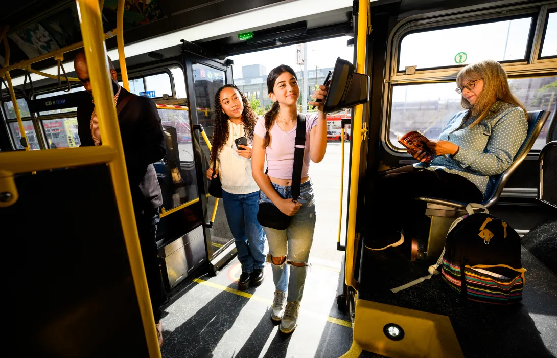 Two teens scanning their smartphone based transit cards as the board a bus