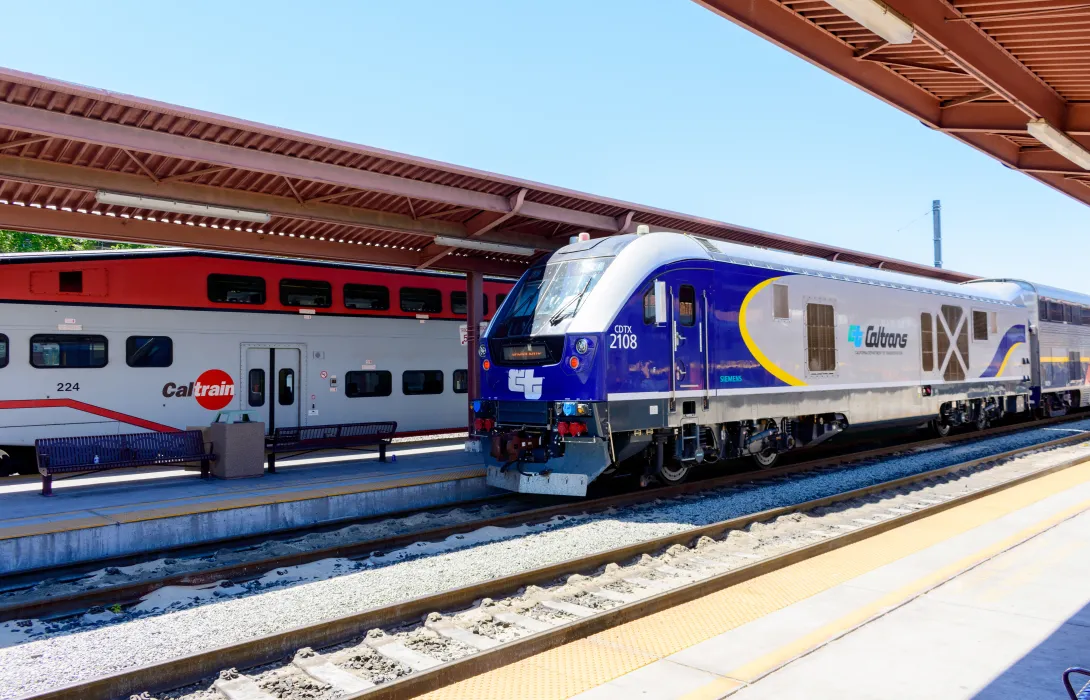 A sleek blue train pulling into a train station next to a red and white train