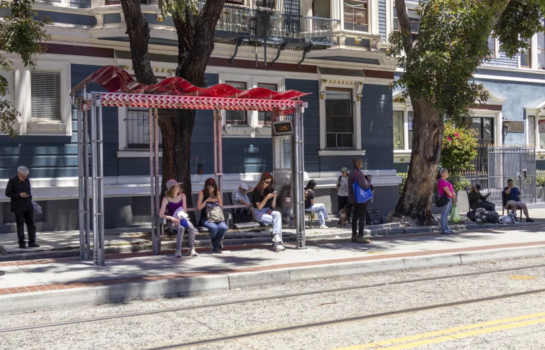 People waiting under a red awning on a bench at a bus stop