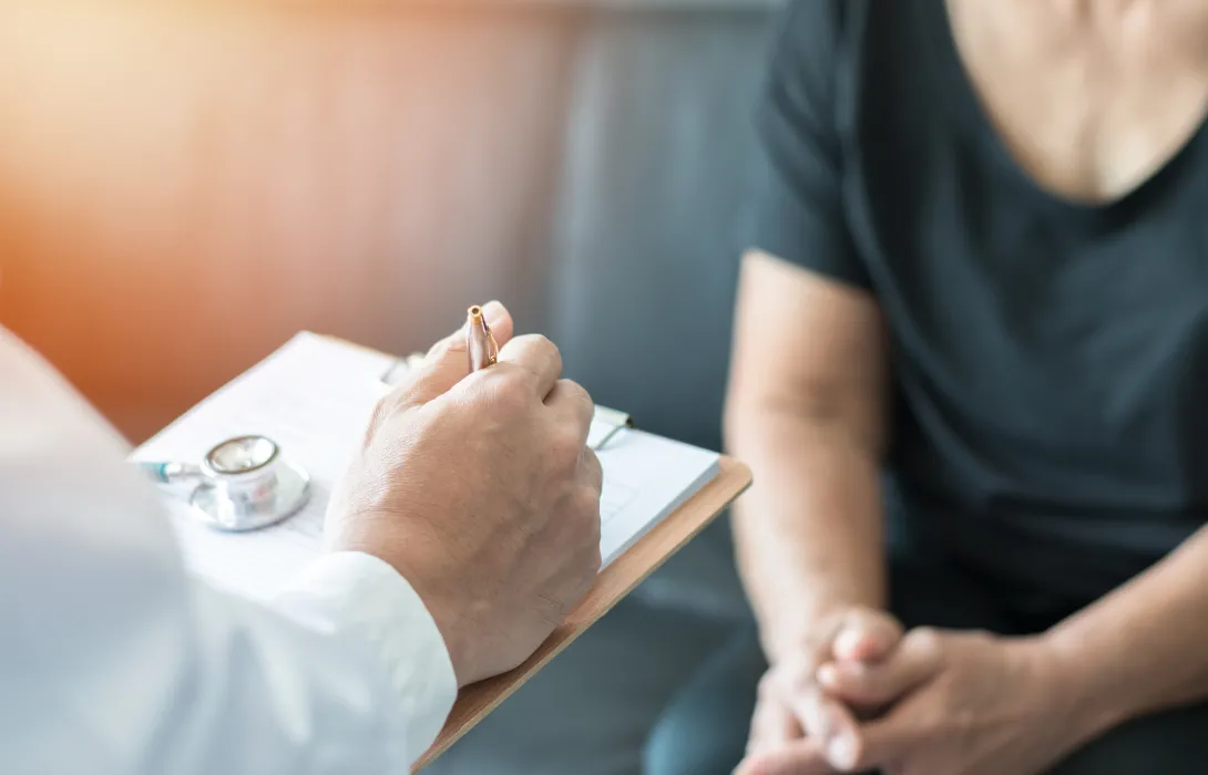 A doctor writing on a clipboard as a patient sits nearby