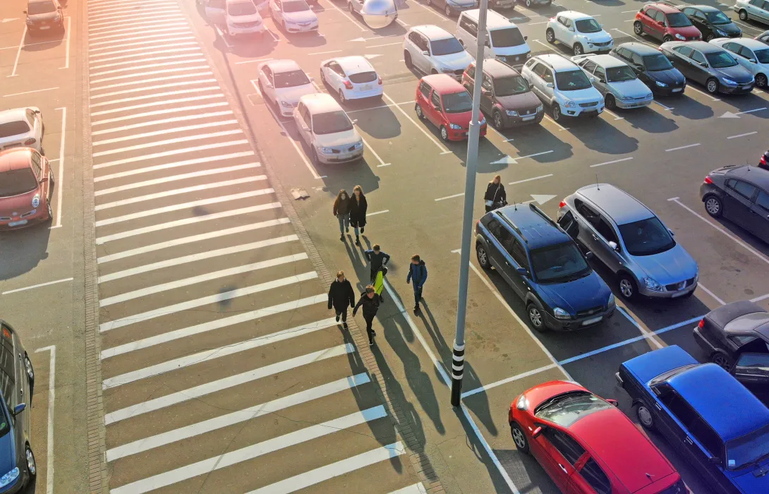 Aerial view of a large parking lot with commuters walking down a crosswalk in the middle