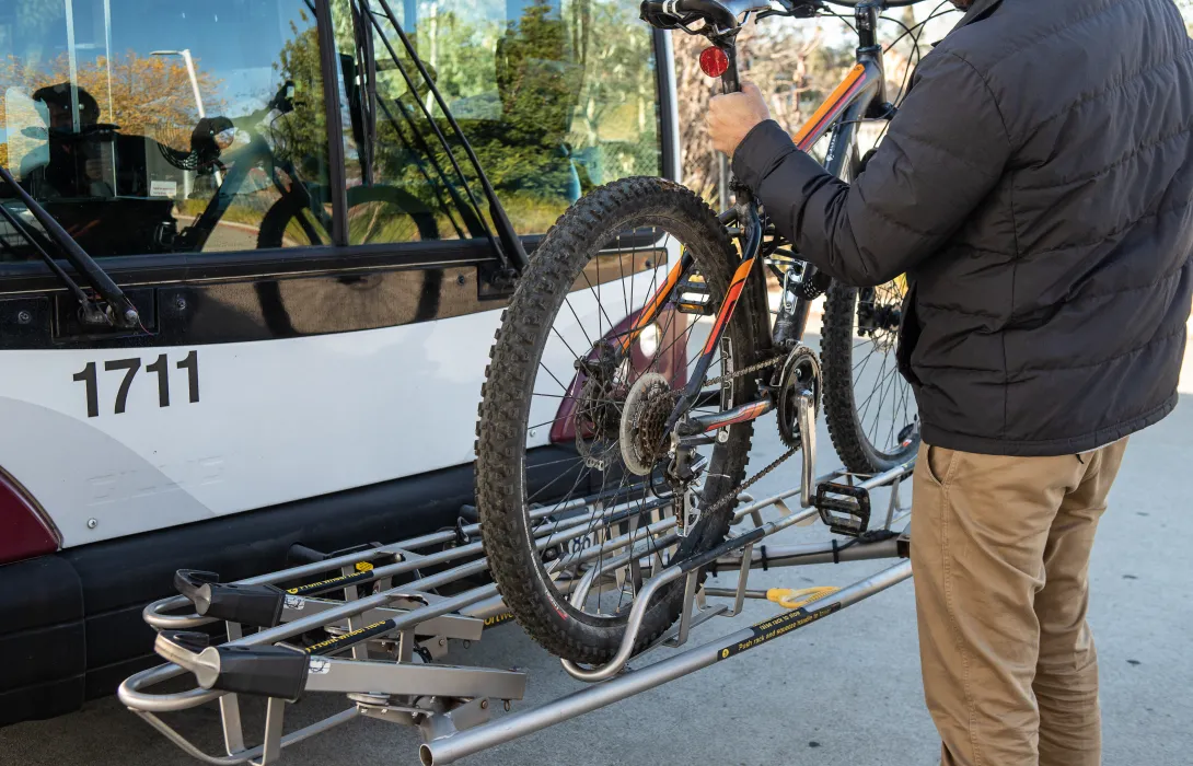 Person loading their bicycle on a bus's bike rack