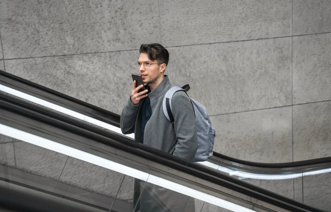 A man speaking into his phone mic while riding an escalator