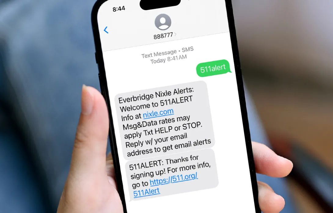 A view of a phone in hand.  The screen shows a text to 888777 with the text 511alert, and a response confirming the subscription, and how to cancel.