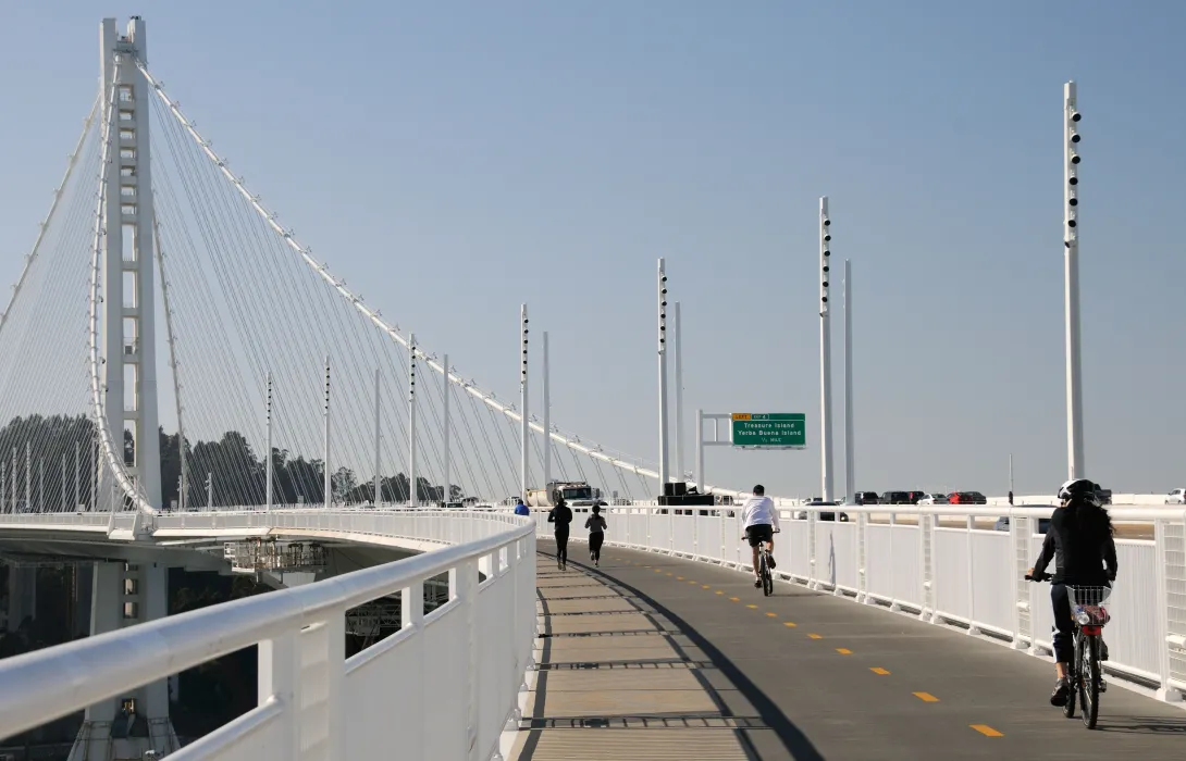 Bicyclists and joggers travel down a dedicated lane along the bay bridge, separate from high-speed traffic.