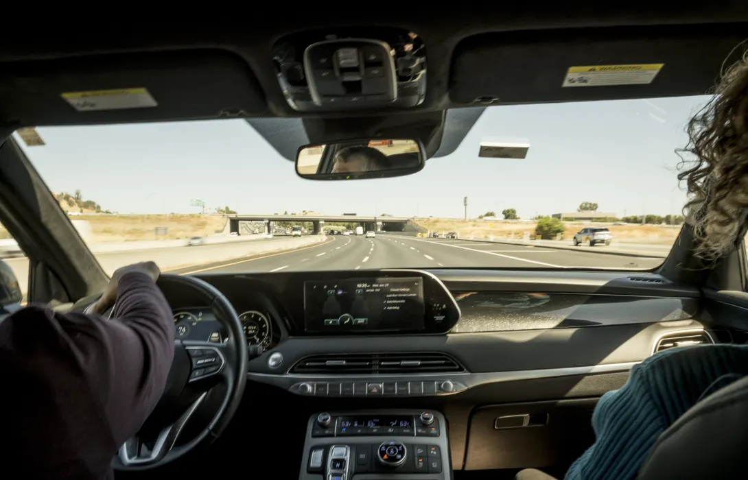 A view out the windshield of a car with two passengers in the front seat, traveling down the highway.